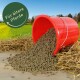 Roter Eimer kippt braune Pferdefutterpellets auf Stroh, grünes Abzeichen mit der Aufschrift 'Für ältere Pferde'.