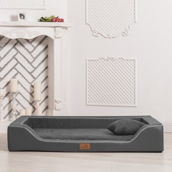 Ein stilvolles graues Hundebett mit einem weichen Kissen und einem kleinen Kissen, in einem hellen Raum mit einem dekorativen Kamin und weißen Wänden platziert.
