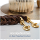 Eine geflochtene braune Leder-Hundeleine mit goldenen Verschlüssen, auf einer strukturierten goldenen Oberfläche platziert, mit dem Text "Handgeflochten in den Niederlanden" darunter.