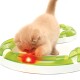 Flauschiges cremefarbenes Kätzchen spielt mit einer grünen runden Spielbahn, in der ein rot leuchtender Ball rollt.