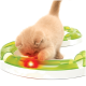 Flauschiges cremefarbenes Kätzchen spielt mit einer grünen runden Spielbahn, in der ein rot leuchtender Ball rollt.