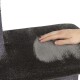 Eine Hand ruht auf einer weichen, plüschigen Oberfläche eines Katzenbaums und zeigt einen Farbverlauf von dunkelgrauem zu hellgrauem Stoff.