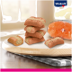Une planche à découper en bois contient cinq friandises pour animaux de compagnie brunes et beiges, une à côté de l'autre, avec du saumon en arrière-plan et le logo Vitakraft.