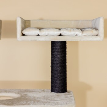 Ein beiger Kratzbaum für Katzen mit einem plüschigen oberen Regal mit weißen Kissen und einem mit schwarzem Sisal umwickelten Kratzbaum.