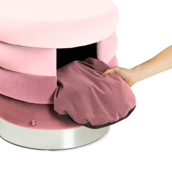 Eine Hand zieht ein weiches, burgunderfarbenes Haustierbett aus einem stilvollen, mehrschichtigen rosa Haustiermöbelstück mit einem silbernen Sockel.