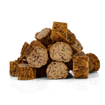 Ein Haufen runder, brauner Haustierfutter-Kibble-Stücke, die auf einer reflektierenden Oberfläche gestapelt sind und ihre strukturierten Oberflächen zeigen.