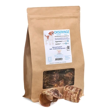 Braune Papiertüte mit Hundeleckerlis, gekennzeichnet mit 'OKSERINGE', mit einem Fenster, das den Inhalt zeigt, mit Rinderringen und einem Hundebild.