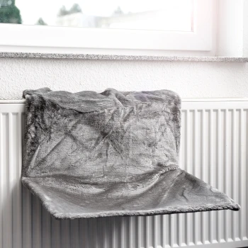 Ein gemütliches graues Haustierbett, das über einem Heizkörper hängt, in der Nähe eines Fensters positioniert, bietet einen warmen Ruheplatz für Haustiere.