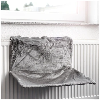 Ein gemütliches graues Haustierbett, das über einem Heizkörper hängt, in der Nähe eines Fensters positioniert, bietet einen warmen Ruheplatz für Haustiere.