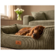 Brauner Hund schläft in olivgrünem Cord-Hundebett mit Lederlabel 'KNUFFELWUFF' in einem gemütlichen Wohnzimmer.