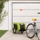 Ein grüner Haustieranhänger, der an einem Fahrrad befestigt ist, mit einer kleinen orangefarbenen Fahne, geparkt auf einem Steinweg neben einer Garagentür.