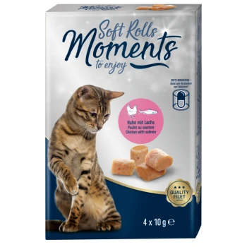 Un chat tigré regarde curieusement une boîte de friandises pour chats "Soft Rolls Moments," avec des saveurs de saumon et de poulet, contenant quatre portions de 10g.