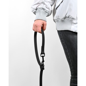 Eine Person in einer hellgrauen Jacke hält eine schwarze Hundeleine in ihrer rechten Hand, die den Clip und das Riemendesign der Leine zeigt.