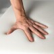 Eine Hand, die in eine weiche, weiße Schaumoberfläche drückt und einen Abdruck hinterlässt, was die Dämpfungseigenschaften des Schaums hervorhebt.