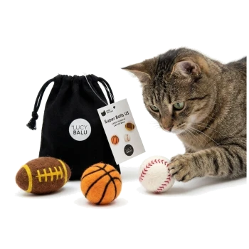 Getigerte Katze stupst einen Filz-Baseball, daneben Basketball und Fußball sowie ein schwarzer Beutel mit der Aufschrift LUCY BALU und Anhänger 'Super Balls US'.