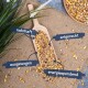 Eine hölzerne Schaufel hält eine bunte Mischung aus Samen und Körnern auf Jute, beschriftet auf Deutsch: "nahrhaft," "artgerecht," "ausgewogen," "energiespendend."