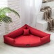 Rotes dreieckiges Haustierbett mit einem kleinen passenden Kissen, platziert in einem hellen Raum mit weißen Wänden und einer Pflanze in der Nähe.