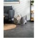Ein kleiner weißer Hund sitzt bequem in einem stilvollen grauen Haustierbett, umgeben von moderner Möbeln und Dekor in einem gemütlichen Wohnzimmer.
