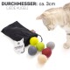 Eine neugierige Katze inspiziert bunte Filzkugeln, die aus einer schwarzen Tasche fallen, beschriftet mit 'Filzbälle für Katzen.'