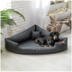Ein schwarz-tanfarbener Hund entspannt sich auf einem modernen, dreieckigen Haustierbett in einem hellen, gemütlichen Raum mit einer Pflanze und weichen Decken im Hintergrund.