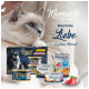 Eine flauschige graue Katze sitzt neben einer "Moments Diamond" Katzenfutterbox mit dem Text "Momente zum Genießen" und "Meine Portion Liebe."