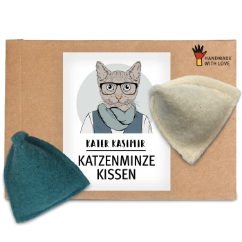 Eine Pappverpackung mit einem Etikett mit dem Text "KATER KASIMIR KATZENMINZE KISSEN" und zwei Katzenminzkissen, eines in Teal und eines in Creme.