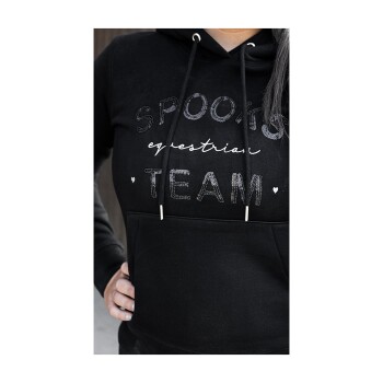 Eine Nahaufnahme einer Person, die einen schwarzen Kapuzenpullover mit dem Text "SPOOKY equestrian TEAM" in glänzenden Buchstaben trägt, mit einer Fronttasche.