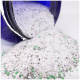 Eine Nahaufnahme eines blauen Glases, das weiße und graue Haustierstreu mit kleinen grünen Granulaten auf eine weiße Oberfläche verschüttet.