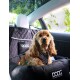 Ein Hund in einem gepunkteten Geschirr sitzt in einem Autositz mit einem schwarzen, gesteppten Bezug, auf dem das "DOOG"-Logo zu sehen ist.
