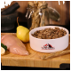 Weißer Futternapf mit der Aufschrift „Tacrenberg“ gefüllt mit Hackfleisch, roher Hähnchenbrust, Birne und Hundeleckerlis auf Holzbrett.