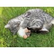 Un chat tigré gris joue sur de l'herbe verte, câlinant un petit jouet en peluche ressemblant à un mouton, avec ses pattes enroulées autour.