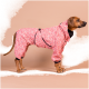 Brauner Hund trägt einen rosa Tarnmuster-Regenanzug mit Kapuze und schwarzem Besatz, steht vor beigem Hintergrund.