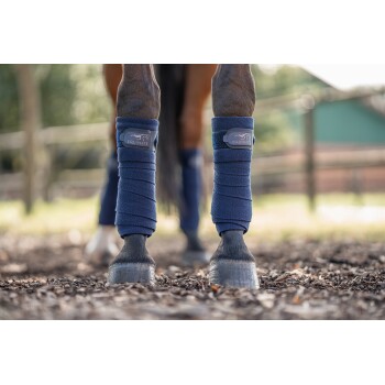 Nahaufnahme von Pferdebeinen, die in blauen Equinate-Beinwickeln eingewickelt sind, mit den Hufen des Pferdes und der umgebenden natürlichen Umgebung.