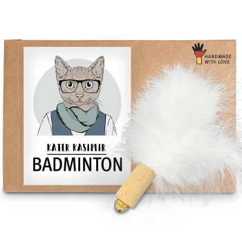 Ein Kartonpaket mit einer Cartoon-Katzenillustration und dem Text "KATER KASIMIR BADMINTON" sowie einem weißen Feder-Spielzeug, das angebracht ist.