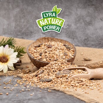 Eine Holzschüssel mit Samen und Körnern, die auf Jute fällt, mit einem Schaufel in der Nähe und Grünpflanzen. Das Logo "LYRA NATURE POWER" oben.