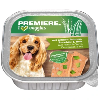 Ein Hund mit langem, welligem Fell lächelt neben einem Behälter mit vegetarischem Hundepâté, das mit "Premiere. Ich ♥ Gemüse" beschriftet ist und grüne Bohnen, Zucchini und Reis enthält.