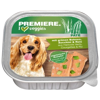 Een hond met lang, golvend haar glimlacht naast een container met vegetarische hondenpaté met het label "Premiere. I ♥ veggies" met groene bonen, courgette en rijst.