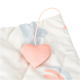 Gros plan d'un lit pour animaux avec un design doux et matelassé dans des couleurs pastel et un jouet en forme de cœur rose attaché par un cordon.