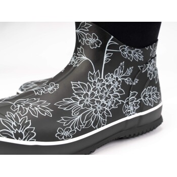 Schwarze Gummistiefel mit weißen Blumenmustern, mit schlankem Design und strukturiertem Sohlen, auf einem weißen Hintergrund präsentiert.