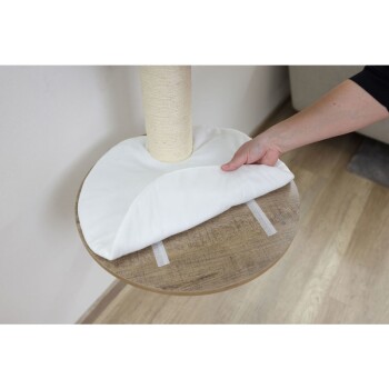 Osoba kładzie biały poduszkę na okrągłej drewnianej platformie drzewka dla kotów, które ma owinięty sizalem słupek do drapania.