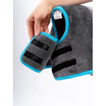 Eine Hand, die einen grauen Haustiermantel mit blauen Akzenten hält, der einen Klettverschluss und ein Etikett mit Produktdetails im Kragen zeigt.