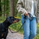 Person hält eine schwarze Seil-Leine und geht mit einem schwarz-braunen Doberman auf einem Waldweg, trägt Jeans und beige Jacke.