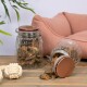 Zwei Glasbehälter gefüllt mit Leckerlis für Haustiere, einer umgekippt und Leckerlis auf eine Holzoberfläche verschüttet, mit einem plüschigen rosa Haustierbett und einem Seilspielzeug in der Nähe.