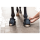 Eine Person befestigt einen schwarzen Hufschuh mit der Bezeichnung "EQUINATE" am Vorderhuf eines Pferdes, der das Design und die Passform des Schuhs zeigt.