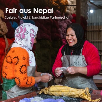 Zwei Frauen in bunten Kleidern arbeiten zusammen in einer Werkstatt, umgeben von lebhaften Wollfasern. Der Text lautet "Fair aus Nepal."