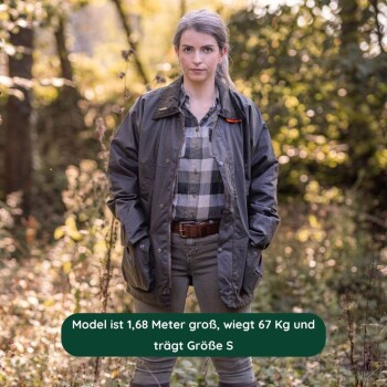 Person trägt eine dunkelgrüne Outdoor-Jacke mit großen Taschen und orangefarbenem Kragen, steht in einem bewaldeten Gebiet.