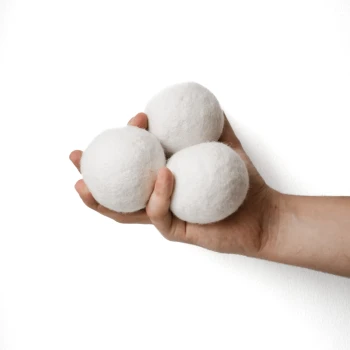 Eine Hand, die drei weiße, gefilzte Wollbälle vor einem schlichten weißen Hintergrund hält.