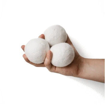 Eine Hand, die drei weiße, gefilzte Wollbälle vor einem schlichten weißen Hintergrund hält.
