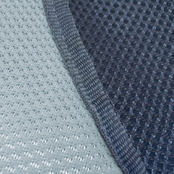 Nahaufnahme eines Haustierbettstoffs mit einer hellgrauen Netzseite und einer dunkelgrauen strukturierten Seite, mit einer sichtbaren Naht zwischen ihnen.