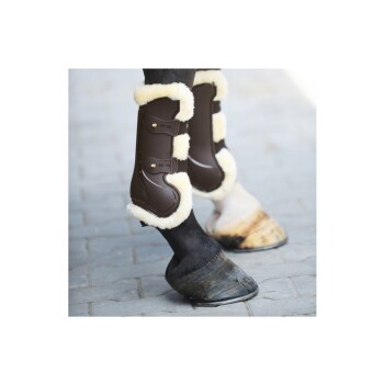 Braune Pferdebeinschoner mit flauschigem weißen Futter an den Beinen eines Pferdes, das auf einer Kopfsteinpflasteroberfläche steht.